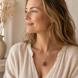 Person wearing a silver crystal cage pendant with a crystal on a delicate chain and neutral clothing in warm natural light.