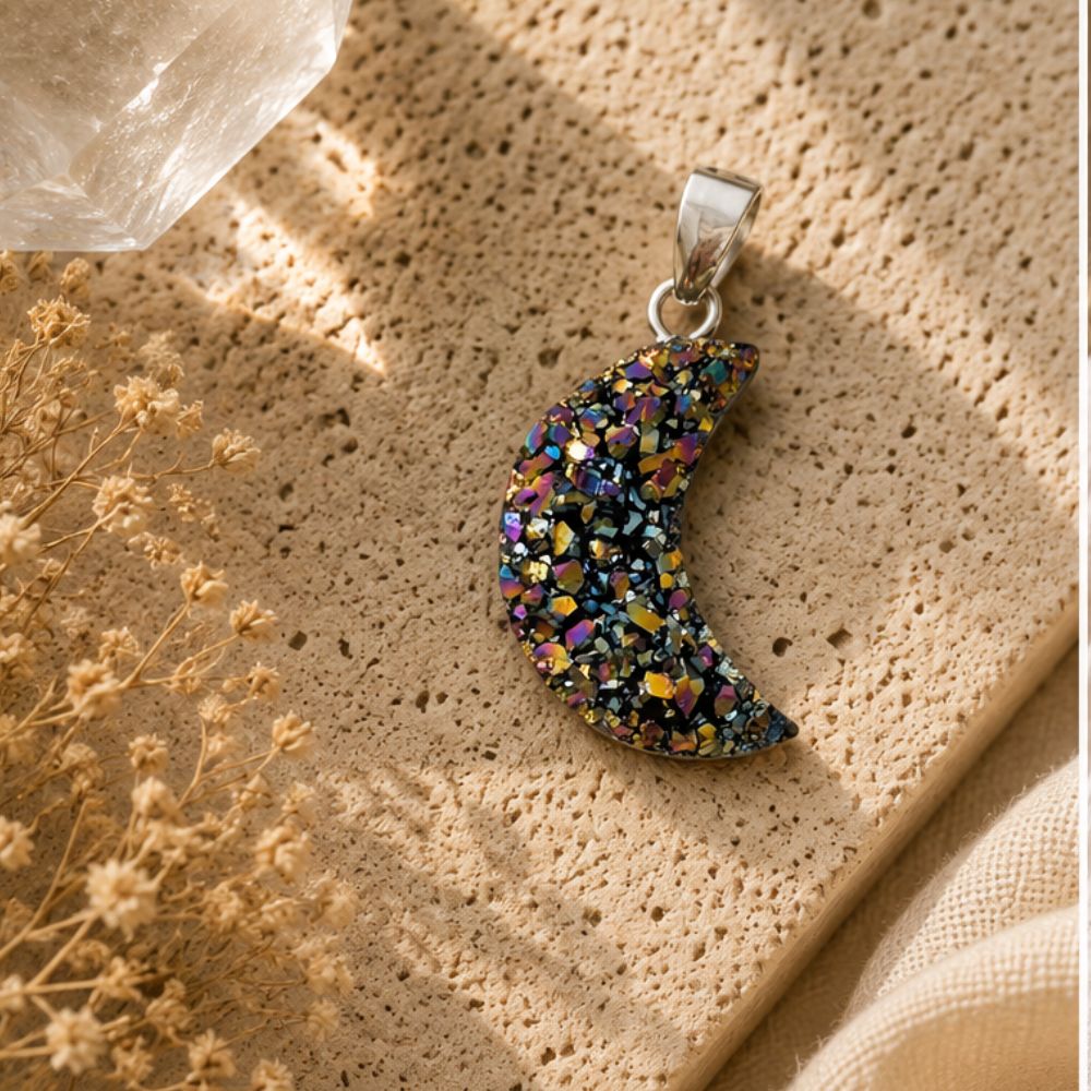 Multicolored crescent moon pendant on a textured beige surface with dried flowers.