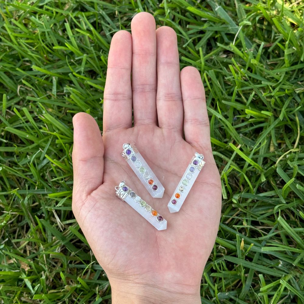 Three small crystal sticks with colorful stones held in a hand on grass
