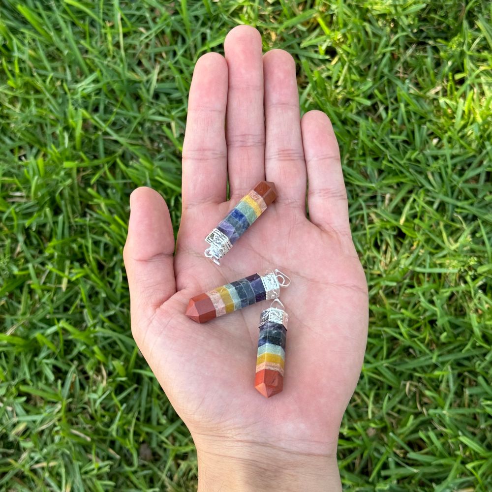 Three small cylindrical crystal bead charms with silver jump rings are resting on an open hand, set against a background of green grass.