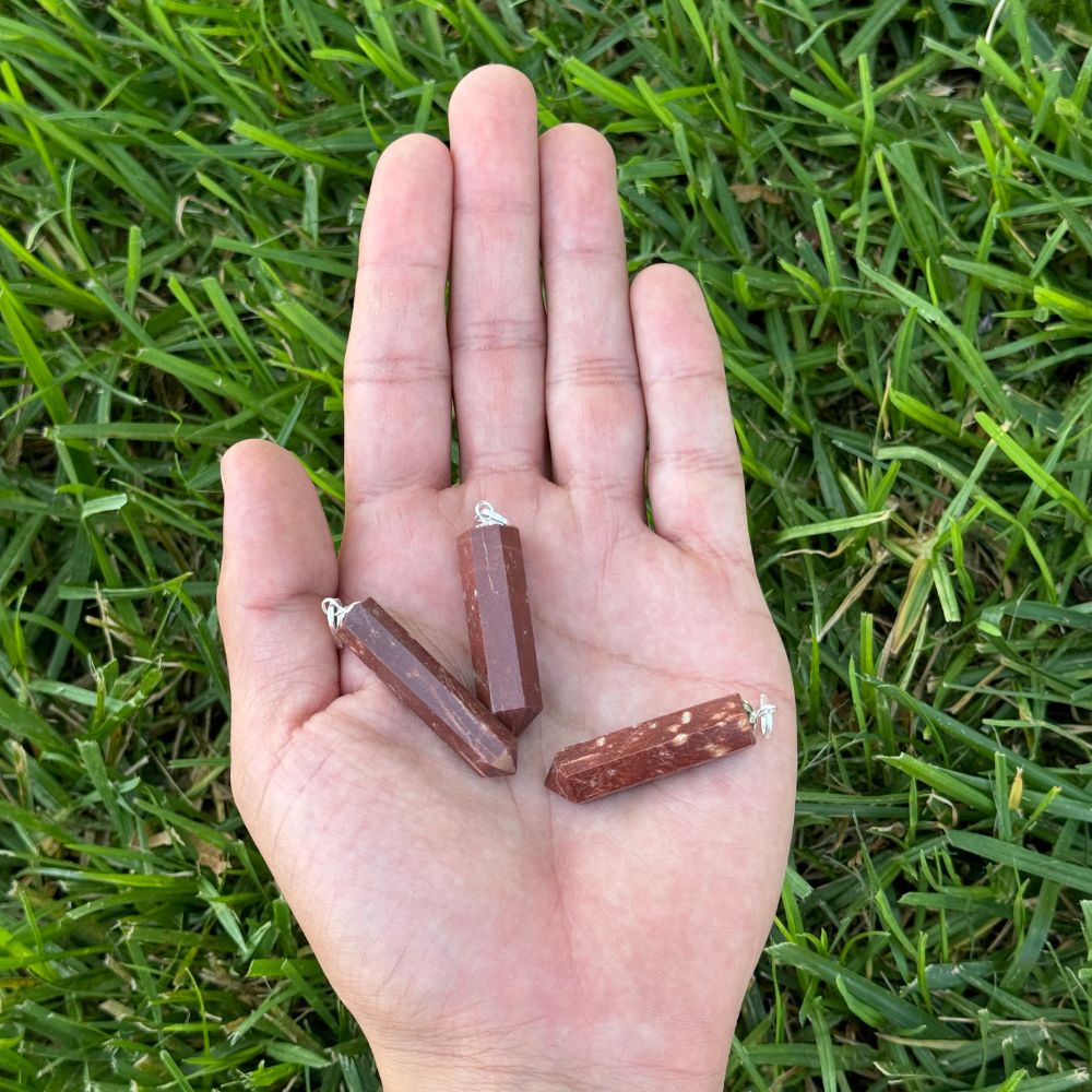 Red Jasper crystal point pendants displayed in the palm of a hand for size reference.