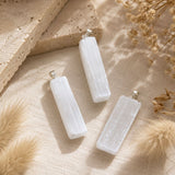 Raw Selenite point pendants displayed on soft linen with natural stone and dried botanicals.