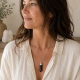 Woman wearing a Shungite point pendant on a silver chain with a white linen shirt.