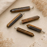 Tiger's Eye crystal point pendants with silver loops on a neutral stone background.