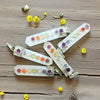 Colorful selenite pendants with gemstones on a wooden surface surrounded by small yellow flowers.