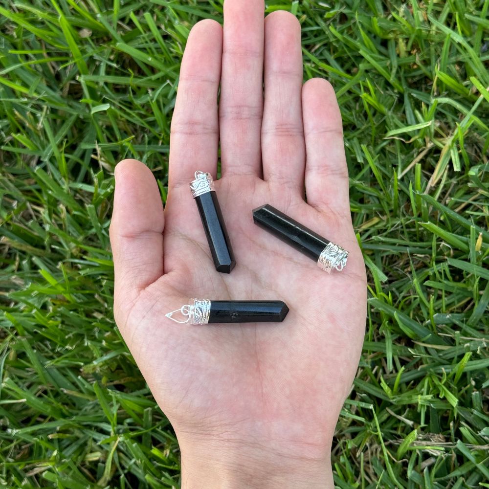 Three Shungite point pendants displayed in the palm of a hand.