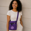 Woman wearing a purple crossbody bag with a logo against a beige wall