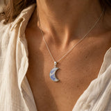 Rainbow moonstone crescent moon sterling silver pendant worn on a necklace.