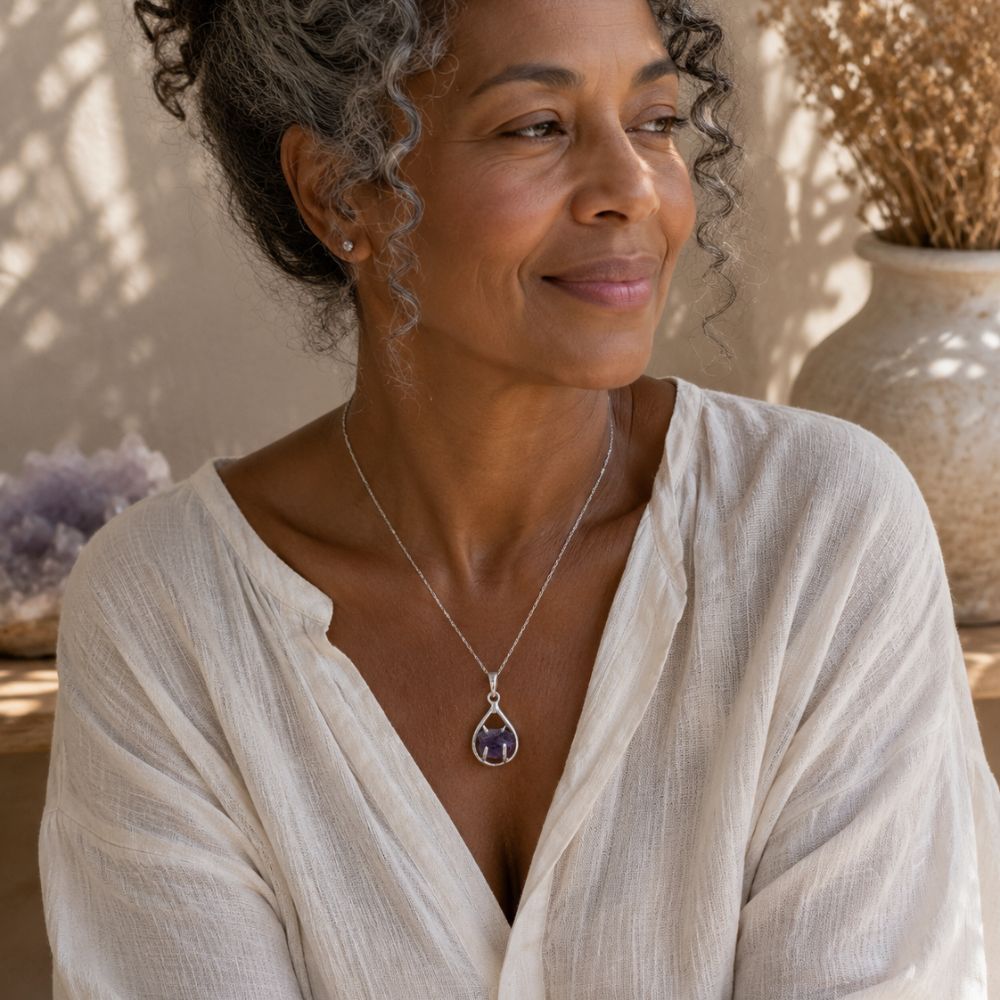 Woman wearing a raw amethyst teardrop pendant in a polished silver setting on a delicate chain with a relaxed linen blouse in soft natural light.