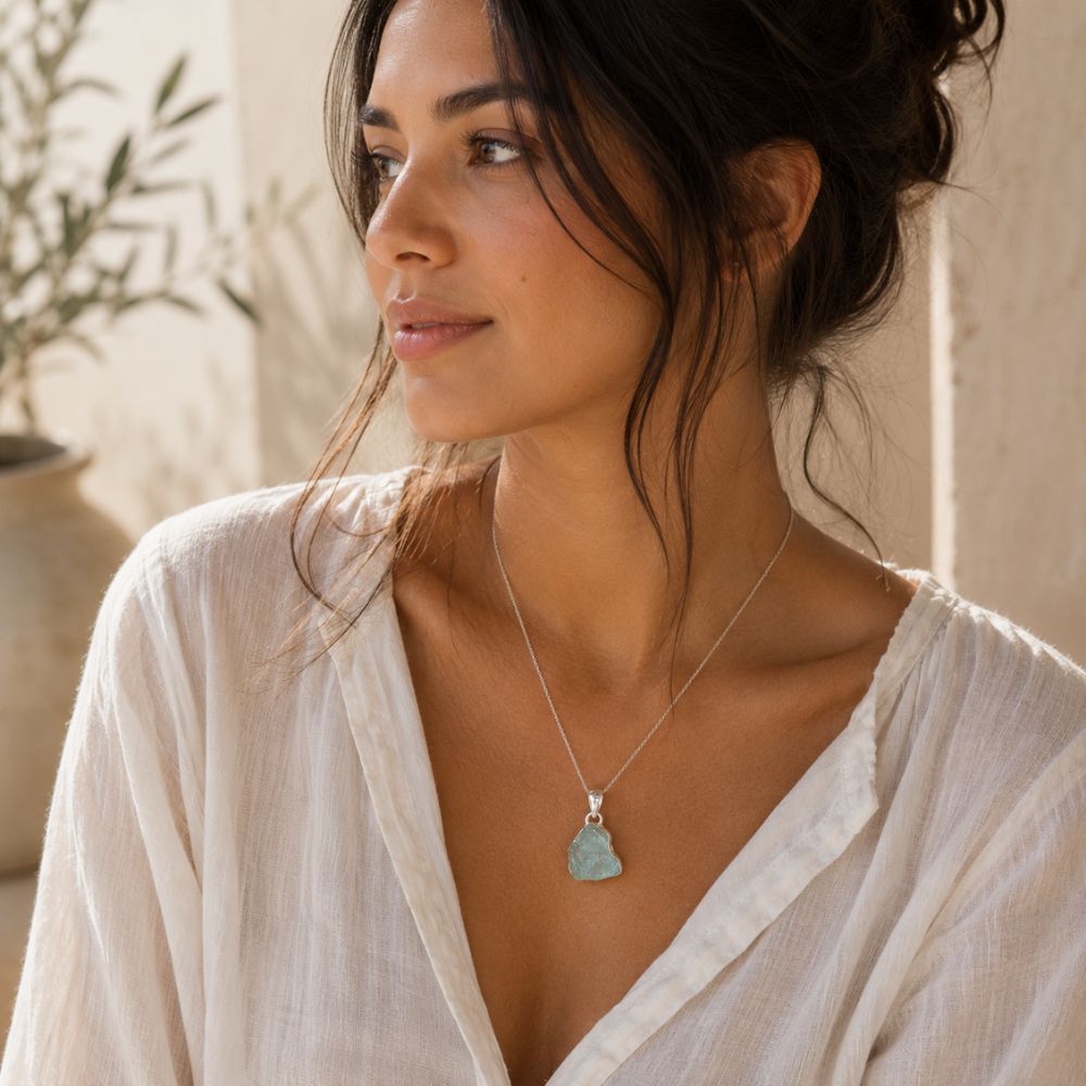 Woman wearing a raw aquamarine pendant on a delicate silver chain with an ivory linen blouse in soft natural light.