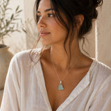 Woman wearing a raw aquamarine pendant on a delicate silver chain with an ivory linen blouse in soft natural light.