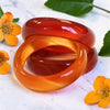Two Carnelian Rings stacked together on a light marble-like surface, surrounded by small yellow flowers and green leaves.