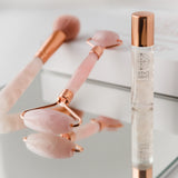 Rose gold facial roller and bottle of Skinesis Elements on a light background