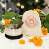 Sacral Chakra Singing Bowl in Pouch surrounded by marigold flowers and green leaves.