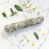 Sage bundle on a marble surface with scattered leaves and flowers