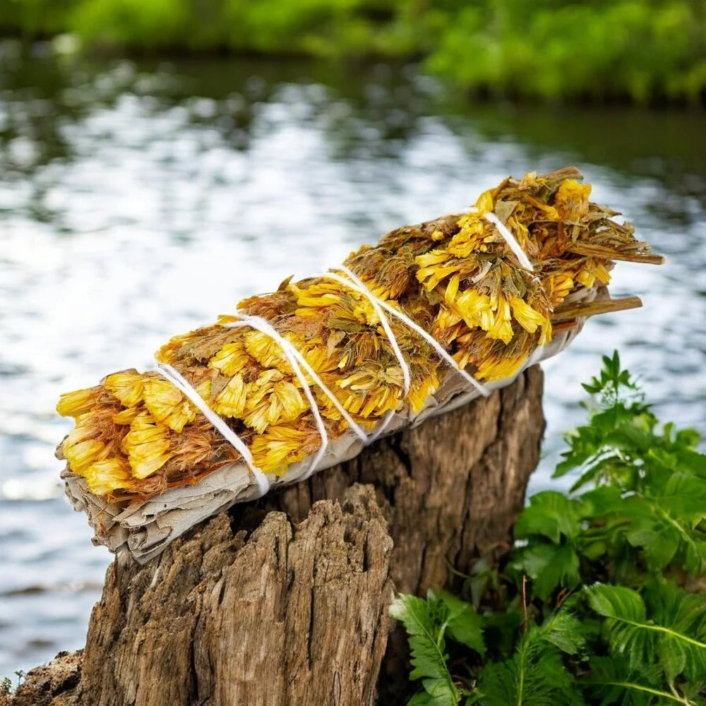 Bundles of yellow flowers tied together with sage on a wooden log with a natural background