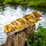 Bundles of yellow flowers tied together with sage on a wooden log with a natural background