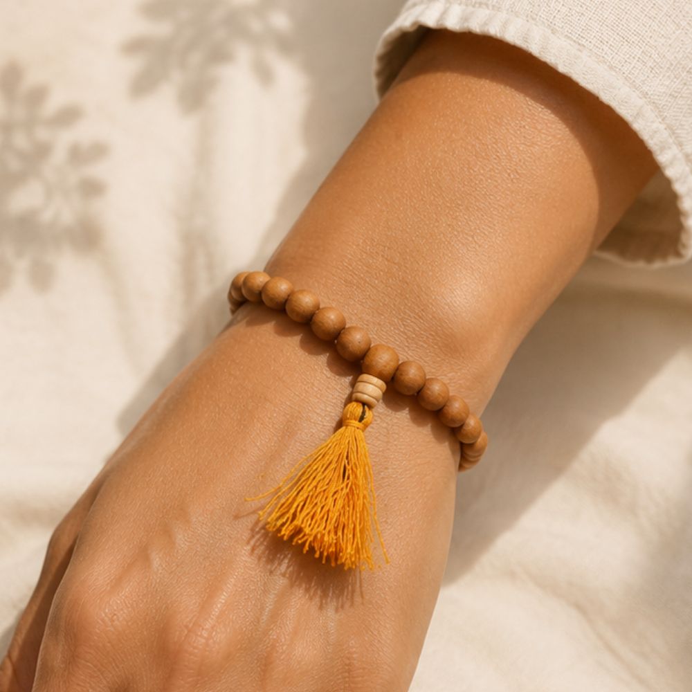 Wooden beaded bracelet with a yellow tassel on a wrist against a neutral background