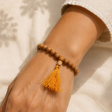 Wooden beaded bracelet with a yellow tassel on a wrist against a neutral background