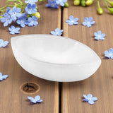 Selenite boat bowl on a wooden surface with small blue flowers around