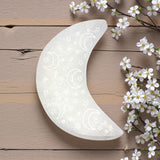 Decorative moon-shaped selenite charging plate with floral design on a wooden surface with white flowers.