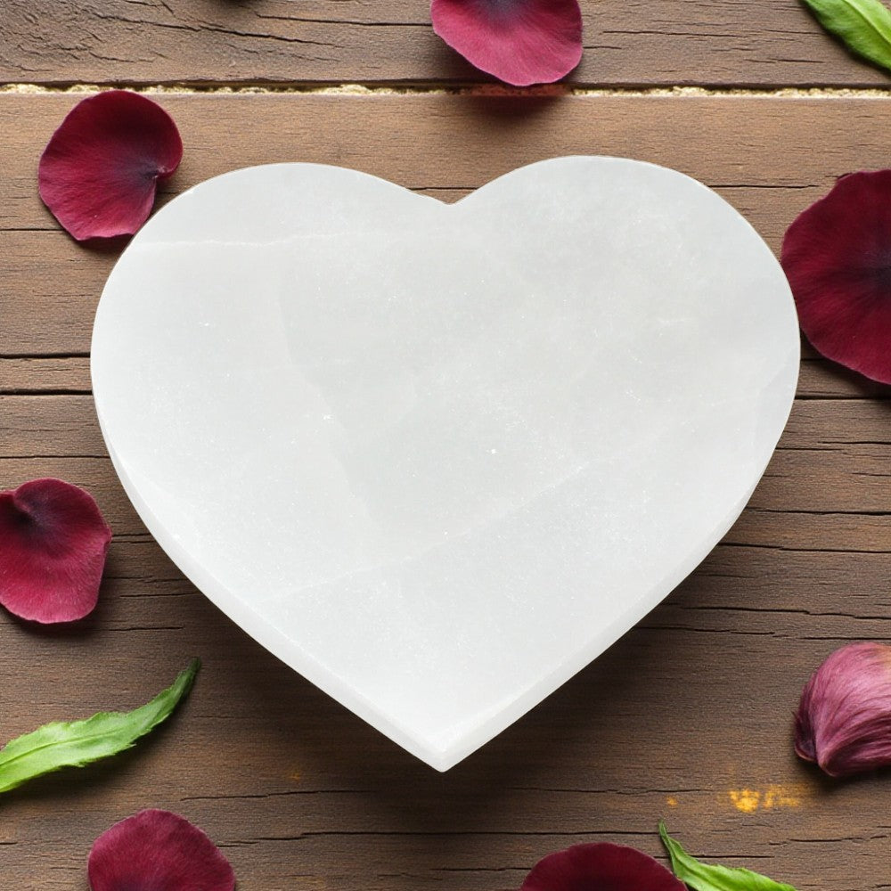 Heart-shaped selenite on a wooden surface with red flower petals