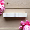 Rectangular white selenite charging bar on a wooden surface with pink flowers