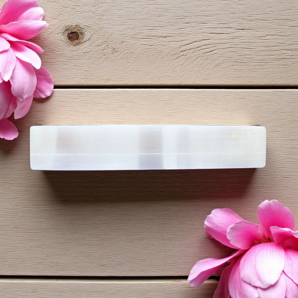 Rectangular white selenite charging bar on a wooden surface with pink flowers