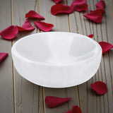 White selenite bowl on a wooden surface with red rose petals