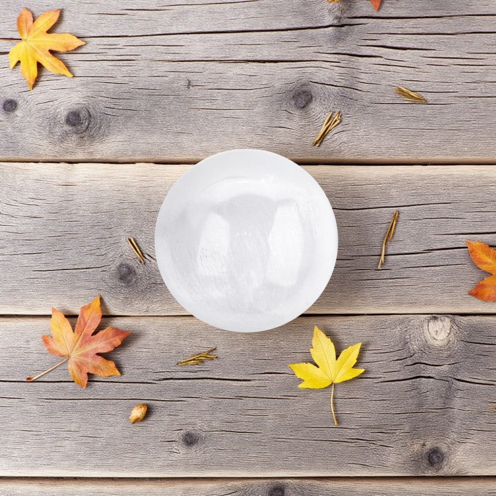 White mini selenite sphere on a wooden surface with autumn leaves