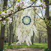 Dreamcatcher hanging from a tree branch with flowers in a park setting