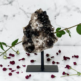 Smoky Quartz Cluster on Stand on a stand with flowers and leaves on a marble background