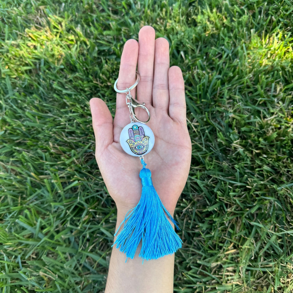 Hand holding a keychain with a blue tassel against a grass background