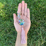 Hand holding a colorful keychain with a tassel against a grass background