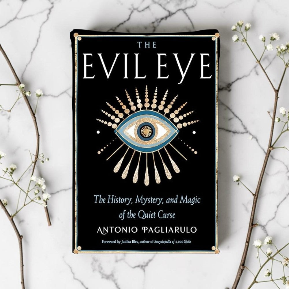 Book cover of 'The Evil Eye' on a marble surface with decorative branches.