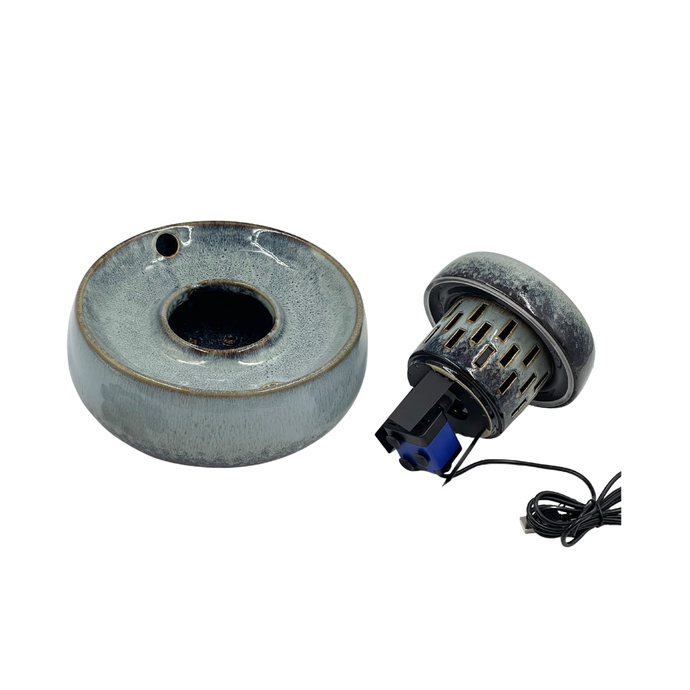 A ceramic ring-shaped vessel with a glossy speckled gray and blue glaze, shown alongside a small black and blue mechanical component with a black wire on a plain white background.