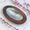 Wooden shell dish with a large shell on a marble surface with pink flowers.