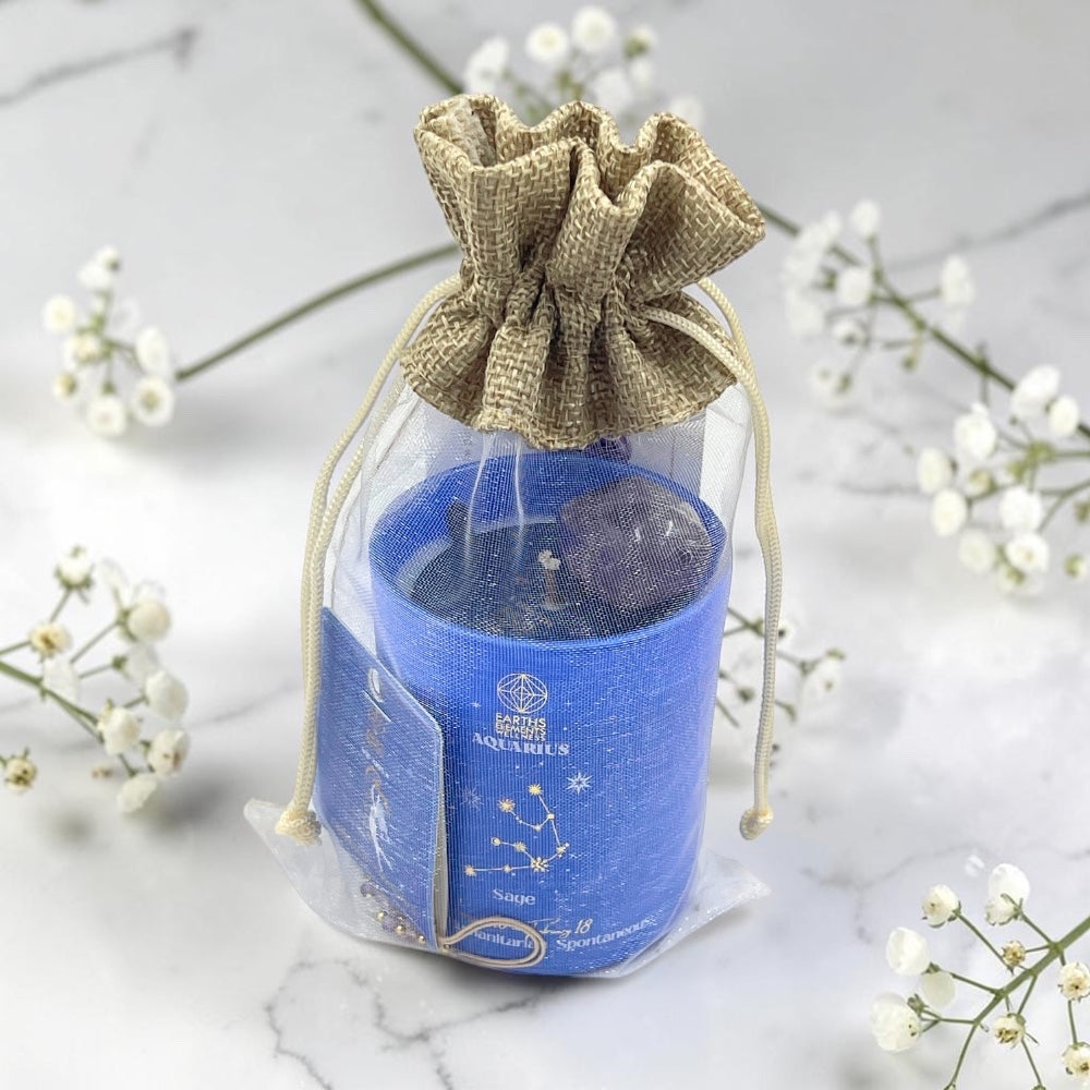 Blue candle in a glass jar with a drawstring bag on a marble surface with white flowers.