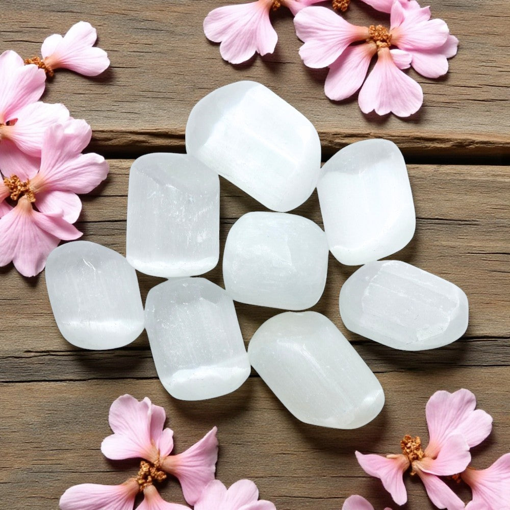White tumbled selenite on a wooden surface with pink flowers
