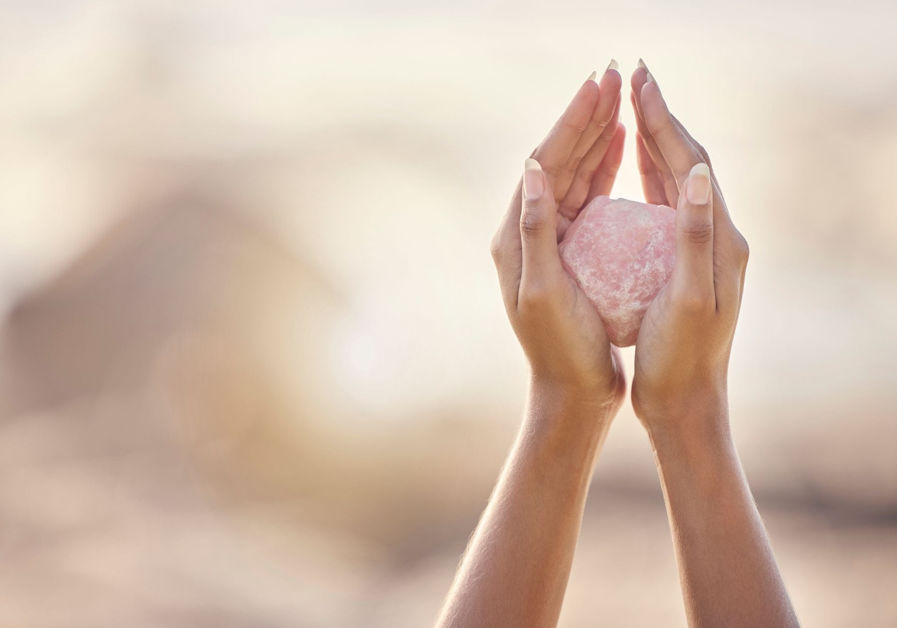 hands holding up a raw piece of rose quartz