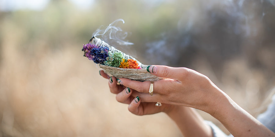 Hands holding an abalone shell with a burning chakra sage bundle