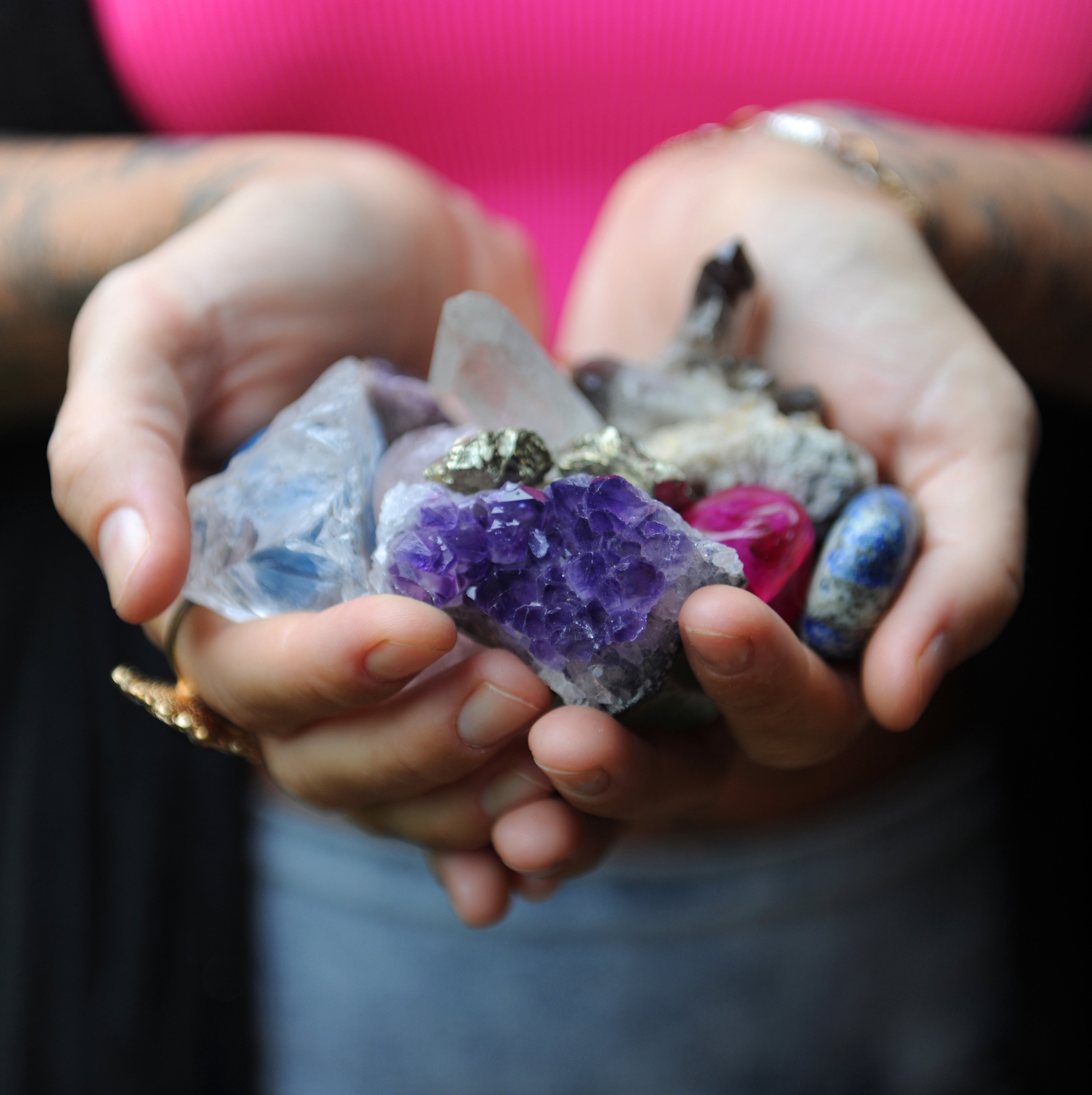 hands holding a variety of raw and tumbled crystals