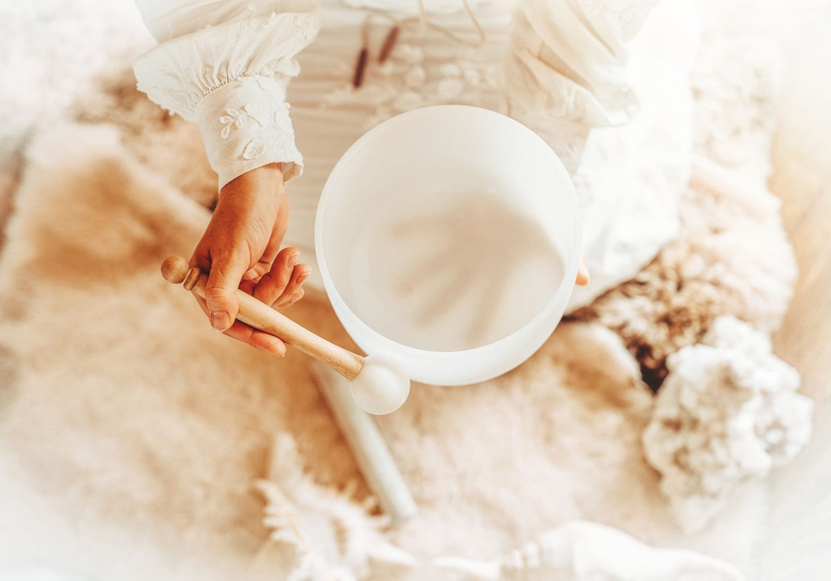 hands playing a white crystal singing bowl. 