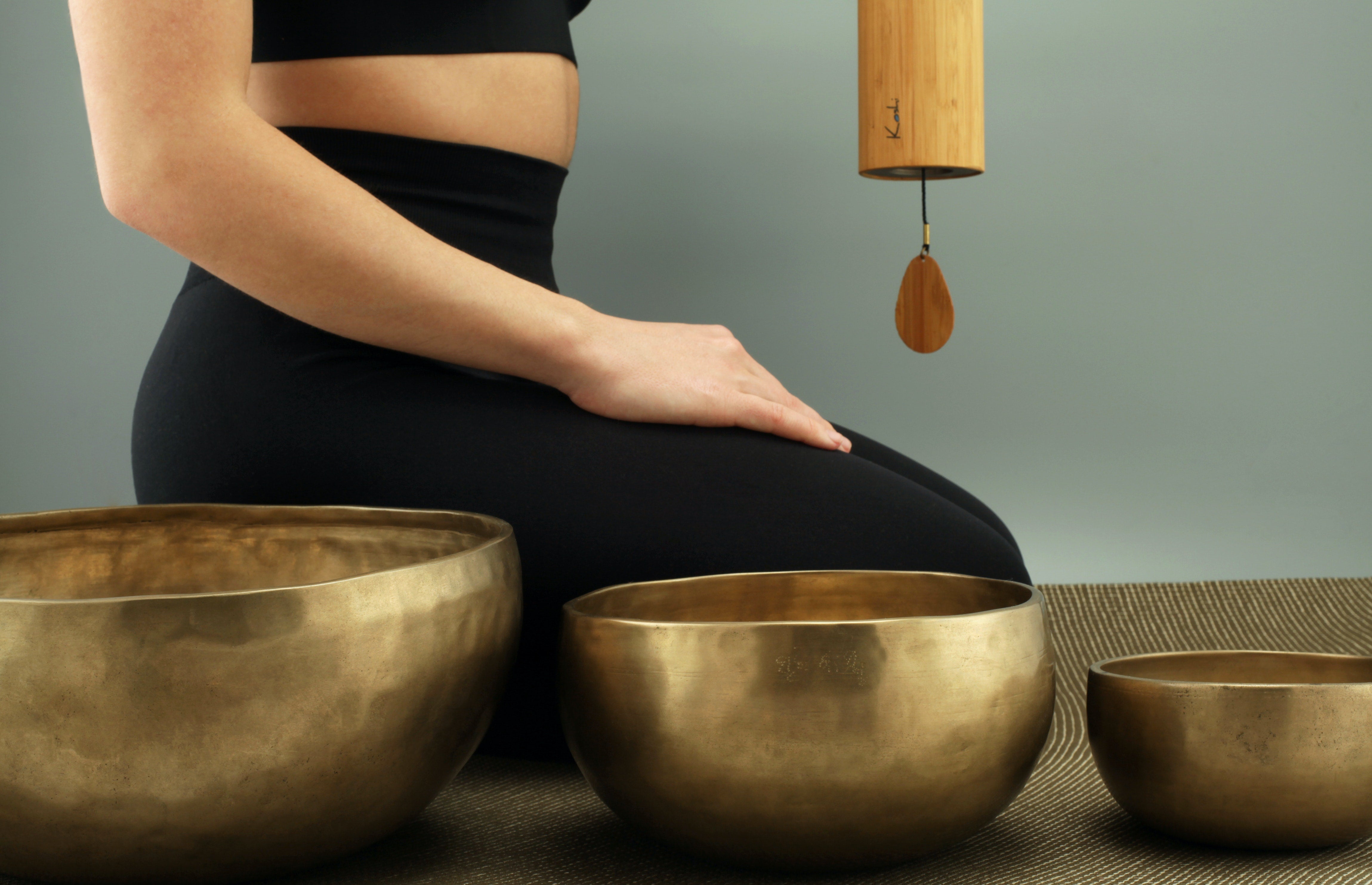 lower part of a sitting woman behind three metal singing bowls