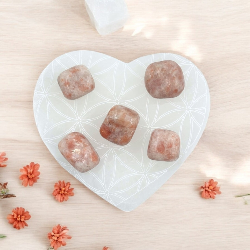 heart shaped selenite coaster with sunstone tumbles on it.