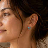 Woman wearing abalone butterfly silver stud earrings with a soft ivory top.