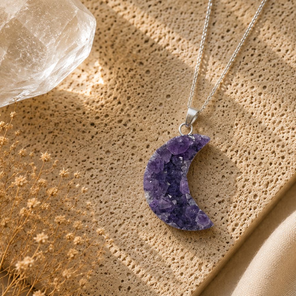Purple amethyst crescent moon necklace on a textured beige surface with dried flowers.