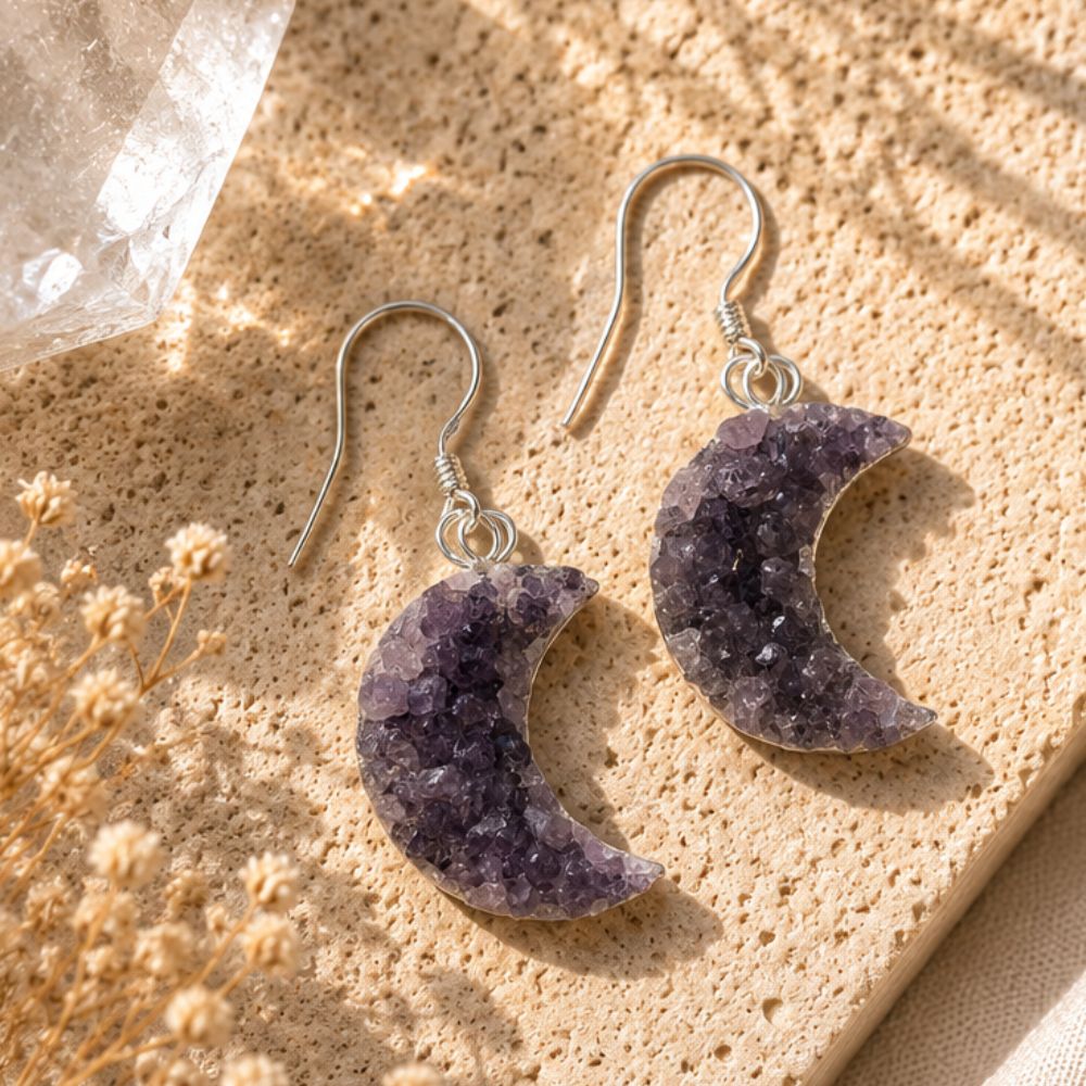 Crescent moon-shaped earrings on a textured surface with dried flowers.