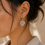 Close-up of a person wearing a sparkling heart-shaped earring with a blurred background