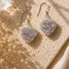 Heart-shaped earrings on a textured beige surface with dried flowers.